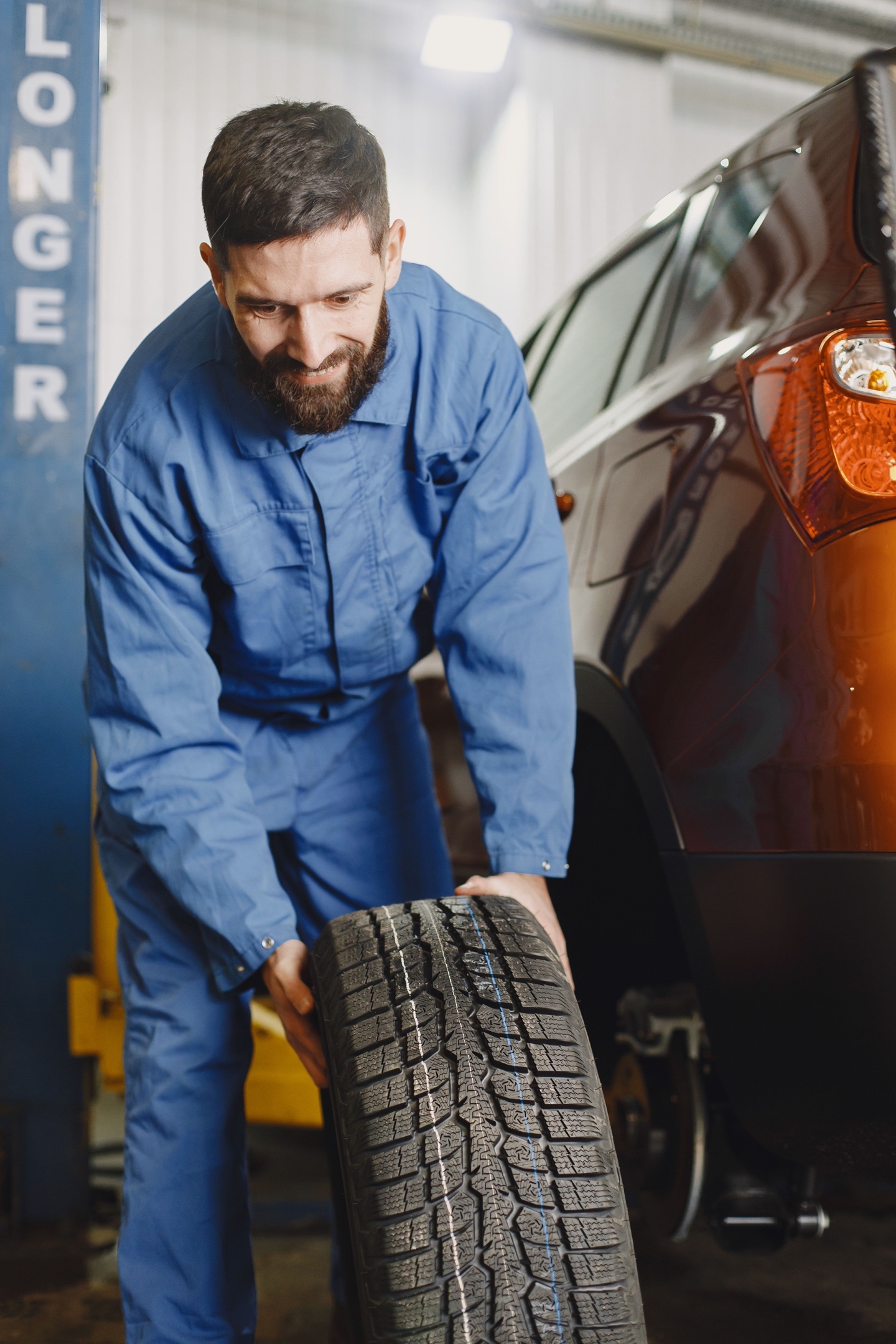 Mechanic rolling a winter tire toward a car in a repair shop